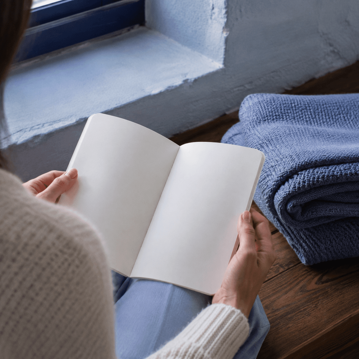 Teacher holding an open blank notebook beside folded mineral-blue blankets
