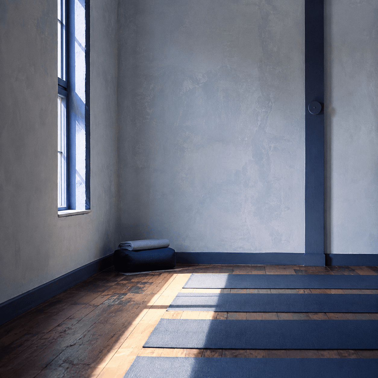 Morning light crossing indigo mats on the studio hardwood floor